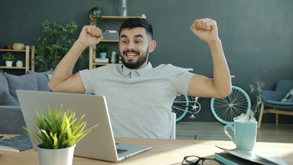 Cinemagraph loop of excited freelancer handsome Arab man getting good news looking at laptop screen at home celebrating success. People and achievements concept.